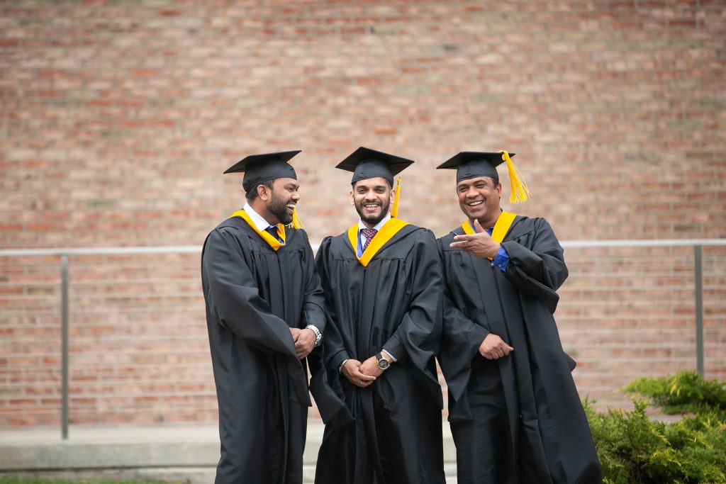 International graduate students laughing together in cap and gown attire